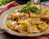 Breite, cremige Pappardelle-Nudeln mit Speck und Kräutern, garniert mit Basilikum.