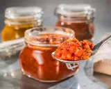 Ein Löffel voll leckerem Tomaten-Chutney, perfekt für Ihr nächstes Tomaten-Chutney-Rezept. Im Hintergrund stehen weitere Gläser mit Chutney.