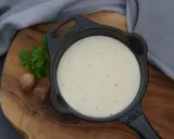 Cremige Béchamelsauce in einer kleinen Gusseisenpfanne, garniert mit Petersilie und Muskatnüssen.