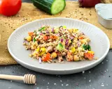 Bunter Quinoa Salat mit Kichererbsen, Tomaten, Gurken und Zwiebeln, garniert mit Zitronenspalten.