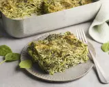 Ein Stück Spinatlasagne auf einem Teller, daneben frische Spinatblätter und eine Gabel. Das Spinatlasagne rezept ist ein Genuss!