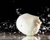 Ein frischer Fior di Latte, der auf einer spiegelnden Oberfläche liegt, umgeben von Wassertropfen und Bokeh-Lichtern.