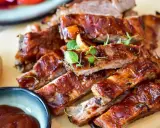 Saftige Spareribs mit glänzender Marinade, garniert mit frischen Kräutern. Dazu eine Schale BBQ-Sauce und eine Kartoffel.