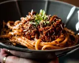 Eine Schüssel mit herzhaftem Pasta al Ragu, garniert mit frischen Kräutern und geriebenem Käse.