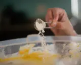 Eine Hand streut Natron aus einem Löffel in eine Schüssel mit Teig. Perfekt für das Backen!