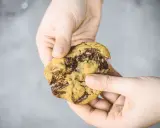 Hände halten einen weichen Chocolate Chip Cookie, der gerade zerbrochen wurde. Das Innere ist voller geschmolzener Schokolade. Ein perfektes Cookies Rezept weich.