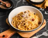 Ein Teller Spaghetti Carbonara, garniert mit Parmesan und schwarzem Pfeffer. Perfekt für authentische Carbonara Rezepte.
