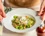 Grüne Bandnudeln mit herzhaftem ragu bianco und Parmesan bestreut, serviert auf einem weißen Teller.