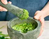 Frische Kräuter werden im Mörser zu einem leuchtend grünen pesto genovese zermahlen.