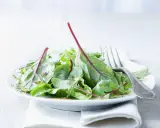 Frischer mangold salat mit roten Stielen, beträufelt mit Dressing, auf einem Teller mit einer Gabel.