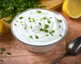 Cremige **sour cream** garniert mit Schnittlauch, daneben Zitronenspalten und ein Löffel.