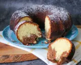 Saftiger weltbester Marmorkuchen, mit Puderzucker bestäubt, auf blauem Teller, ein Stück abgetrennt.
