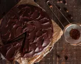 Ein saftiger Nutella Kuchen mit dunkler Schokoladenglasur, ein Stück wurde bereits entnommen. Daneben ein Sieb mit Kakaopulver.