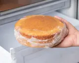 Hand nimmt einen in Frischhaltefolie eingewickelten Kuchen aus dem Kühlschrank, um ihn aufzutauen.