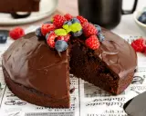 Ein saftiger veganer Schokokuchen mit glänzender Schokoladenglasur, garniert mit frischen Himbeeren und Blaubeeren.