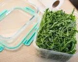 Frischer Rucola Salat in einer Plastikschale, bereit für die Aufbewahrung in einem Glasbehälter.