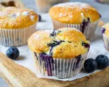 Frisch gebackene Blaubeer Muffins, bestäubt mit Puderzucker, liegen auf einem Holzbrett.