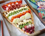 Bunter Fingerfood-Käse-Wurst-Teller in Pizzastückform, perfekt für die Einschulung. Mit Würstchen, Käse, Gurken, Tomaten, Radieschen, Trauben und Salami.