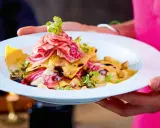 Ein Teller mit Ravioli, garniert mit Streifen von roter Bete und Kräutern. Ein Gericht, das perfekt für "Das perfekte Dinner Rezepte" wäre.