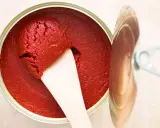 Ein offener Behälter mit leuchtend rotem Tomatenmark, aus dem mit einem Holzspatel eine Portion entnommen wird. Perfekt als Tomatenmark-Ersatz für Saucen und Eintöpfe.