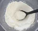 Eine schwarze Löffel hebt eine Portion feines weizenmehl typ 405 aus einer Glasschüssel.
