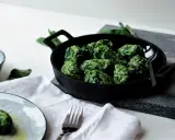 Grüne Malfatti, zubereitet nach einem einfachen Rezept, serviert in einer Gusseisenpfanne. Daneben ein Schälchen mit geriebenem Käse und ein Teller mit den fertigen Malfatti.