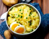 Schüssel mit warmem Kartoffelsalat, garniert mit Schnittlauch und Ei. Ein herzhaftes Gericht, das zum Genießen einlädt.