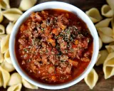 Herzhaftes Ragout alla Bolognese in einer Schüssel, umgeben von ungekochten Muschelnudeln.
