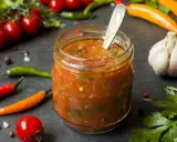 Ein Glas mit würzigem Zucchini-Ketchup, umgeben von frischen Tomaten, Chilis und Knoblauch.