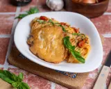 Ein Teller Spaghetti mit Tomatensauce und einem panierten Schnitzel, das ist Piccata. Frisch garniert mit Basilikum.