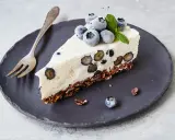 Ein Stück Heidelbeertorte ohne Backen auf schwarzer Platte, garniert mit frischen Heidelbeeren und Minze.