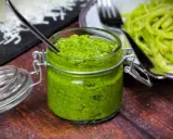 Frisches Rucola Pesto in einem Glas mit Löffel, daneben eine Portion Pasta.