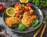 Piccata Milanese mit Pasta und frischen Tomaten, garniert mit Basilikum und Zitrone. Ein köstliches Gericht, das Appetit macht.