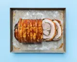 Ein knusprig gebratenes Stück Porchetta, ein italienisches Schweinebraten-Gericht, liegt auf einem Blech.