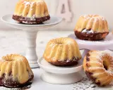Mehrere kleine, mit Puderzucker bestäubte Mini Gugelhupf-Kuchen mit Schokoladenboden stehen auf verschiedenen Etageren.