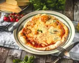 Eine köstliche Pizza Quattro Formaggi mit vier Käsesorten, serviert mit frischen Tomaten und Basilikum auf einem Holztisch.