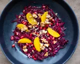 Ein bunter rotkohl salat mit Orangenfilets, Granatapfelkernen und Walnüssen in einer dunklen Schüssel.