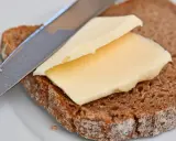 Ein Messer verteilt cremige Butter oder Margarine auf einer Scheibe dunklem Brot.