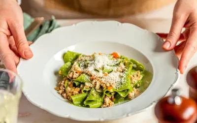 Grüne Bandnudeln mit herzhaftem ragu bianco und Parmesan bestreut, serviert auf einem weißen Teller.