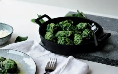 Grüne Malfatti, zubereitet nach einem einfachen Rezept, serviert in einer Gusseisenpfanne. Daneben ein Schälchen mit geriebenem Käse und ein Teller mit den fertigen Malfatti.