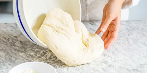 Frischer Teig aus Mehl Typ 00 wird aus einer Schüssel auf eine bemehlte Arbeitsfläche gegeben.