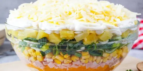 Schichtsalat-Rezept: Bunter Salat mit Ananas, Mais, Schinken, Lauch und Käse in einer Glasschüssel.