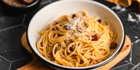 Ein Teller Spaghetti Carbonara, garniert mit Parmesan und schwarzem Pfeffer. Perfekt für authentische Carbonara Rezepte.