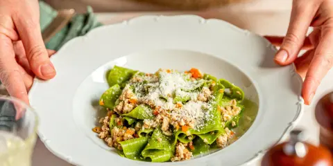 Grüne Bandnudeln mit herzhaftem ragu bianco und Parmesan bestreut, serviert auf einem weißen Teller.