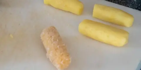 Vier Kartoffelstäbchen liegen auf einem Schneidebrett. Eines ist bereits paniert, die anderen drei warten darauf, dass sie **kroketten selber machen** können.