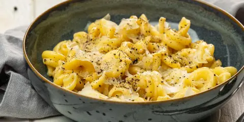 Eine Schüssel mit italienischen Nudeln, bestreut mit Parmesan und schwarzem Pfeffer, serviert auf einem rustikalen Tisch.