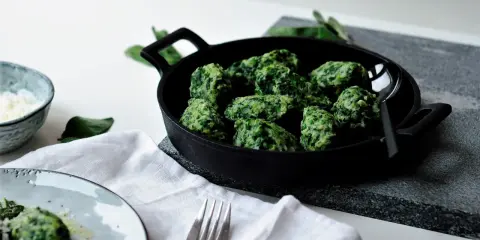 Grüne Malfatti, zubereitet nach einem einfachen Rezept, serviert in einer Gusseisenpfanne. Daneben ein Schälchen mit geriebenem Käse und ein Teller mit den fertigen Malfatti.