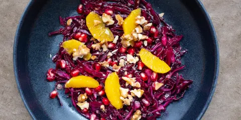 Ein bunter rotkohl salat mit Orangenfilets, Granatapfelkernen und Walnüssen in einer dunklen Schüssel.