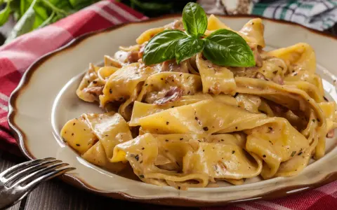 Breite, cremige Pappardelle-Nudeln mit Speck und Kräutern, garniert mit Basilikum.