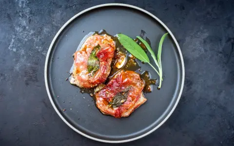 Zwei in Prosciutto eingewickelte Fleischstücke mit Salbei, glasiert und auf einem Teller serviert. Ein köstliches Beispiel für italienische Gerichte.
